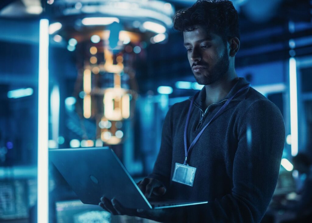 Man with laptop in futuristic blue data center, working on tech.