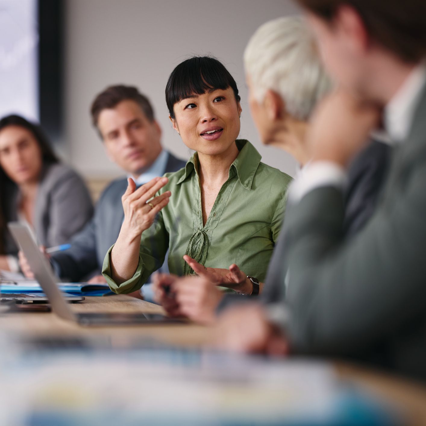Asian businesswoman in green shirt talking at a business meeting with colleagues.